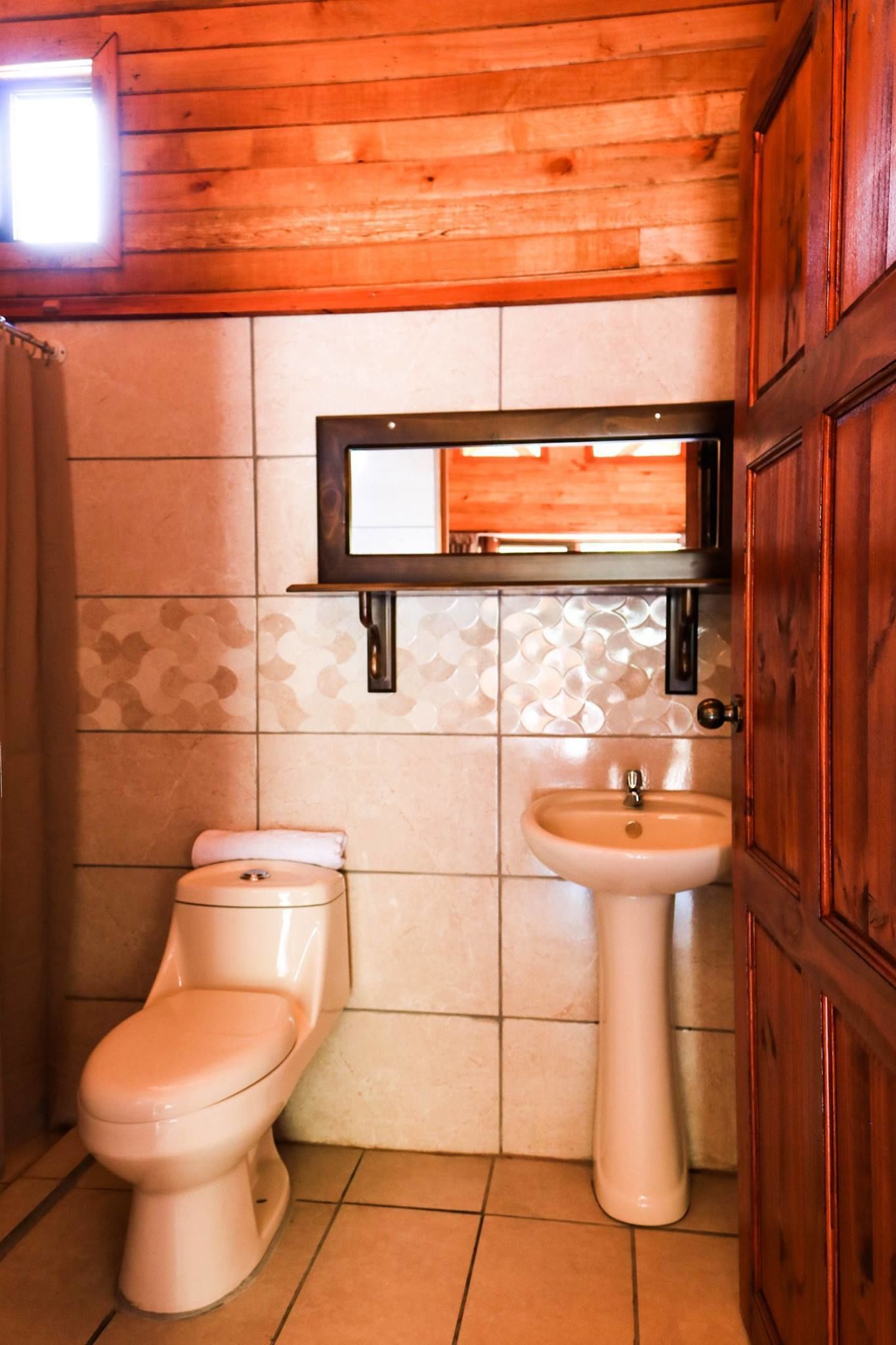 A bathroom with a toilet, sink, and wooden ceiling.