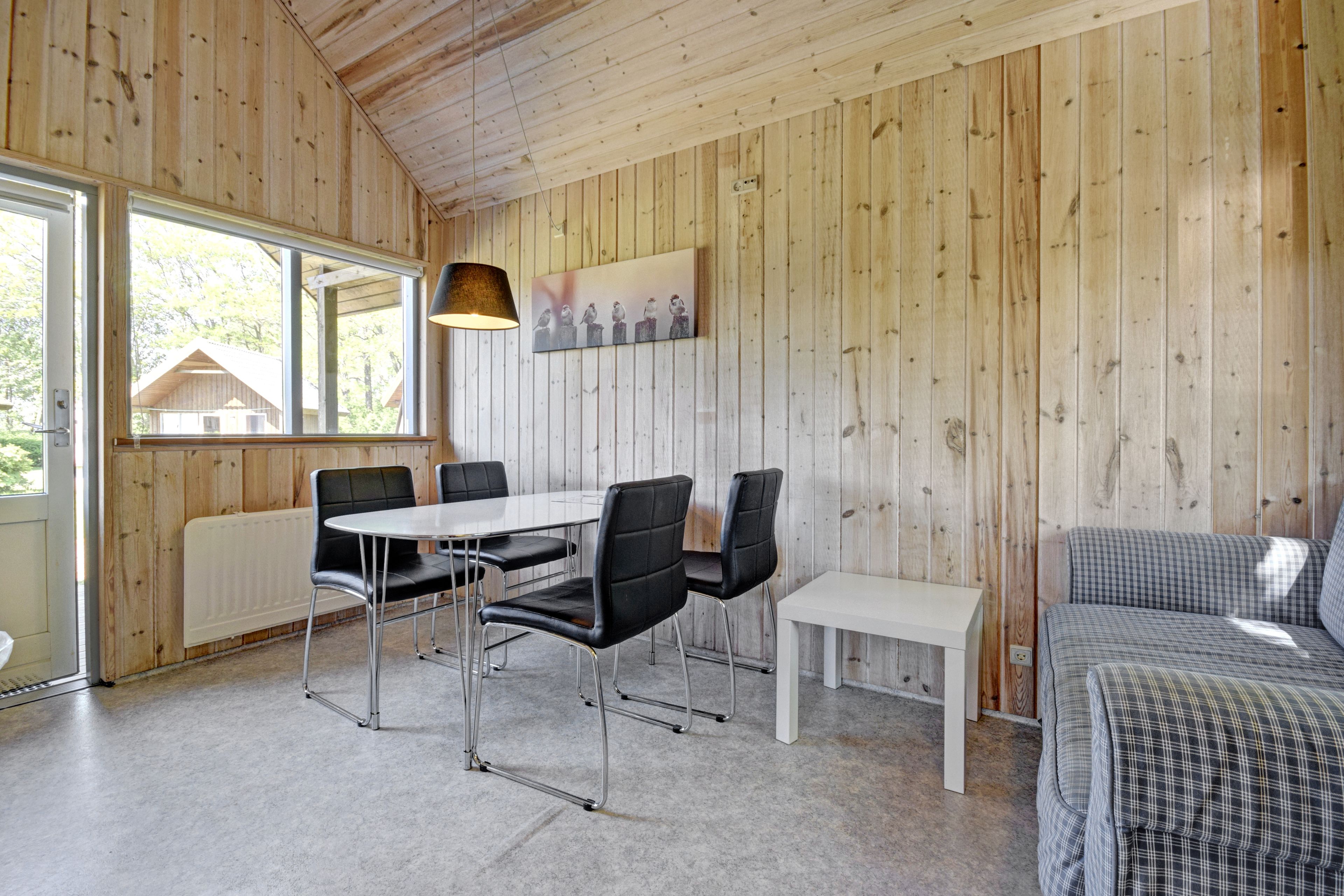 A wooden-paneled room with a dining table, chairs, a bench, and a bed.
