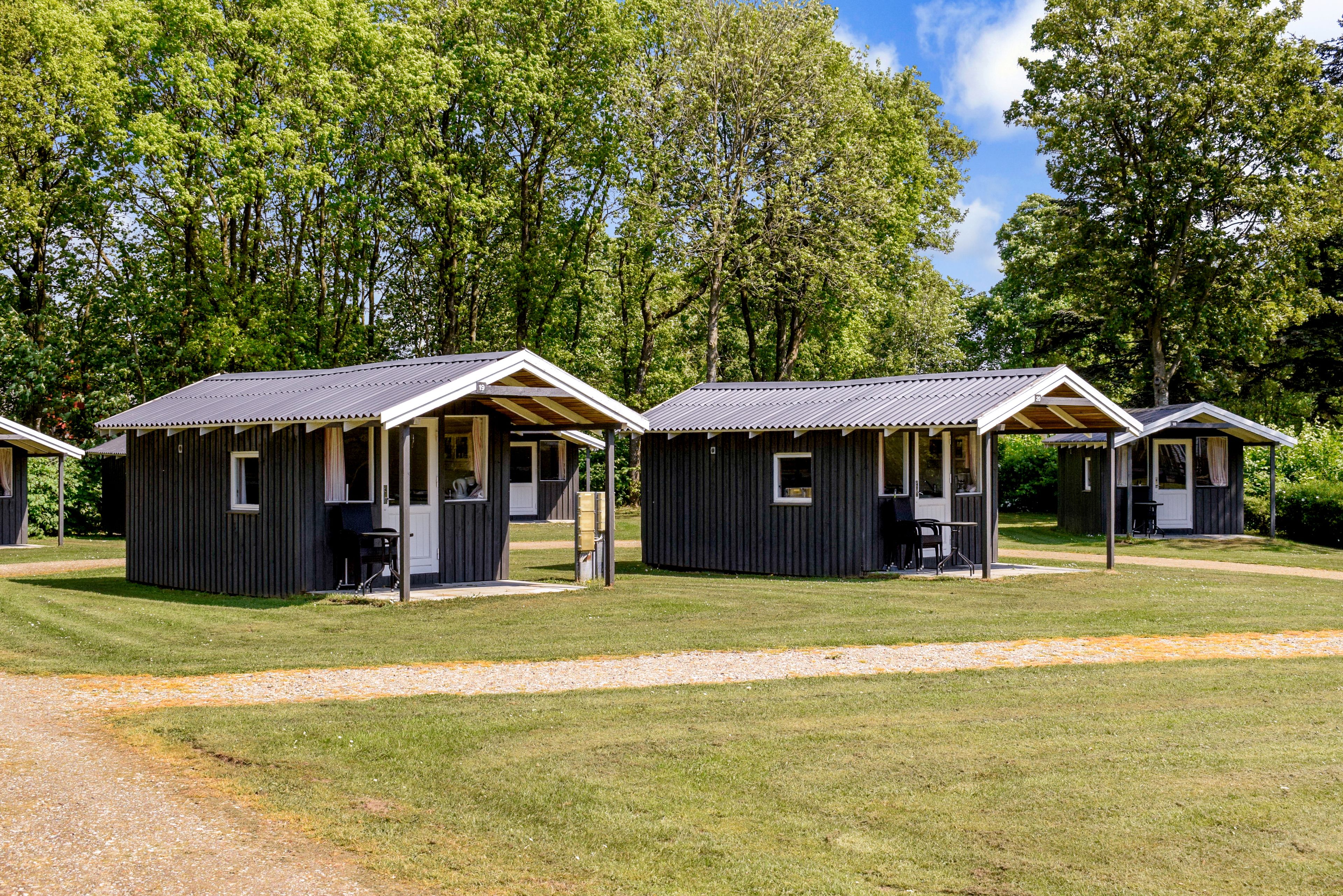 A row of small, dark-colored cabins with wooden beams and a gravel path in front.