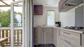 A modern kitchen with wooden cabinets, a gas stove, and a window overlooking a deck. - Jelling Familie Camping (Jelling)