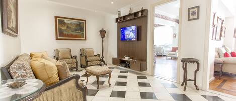 Una sala de estar con piso a cuadros, un sofá, sillones, un televisor y una lámpara.