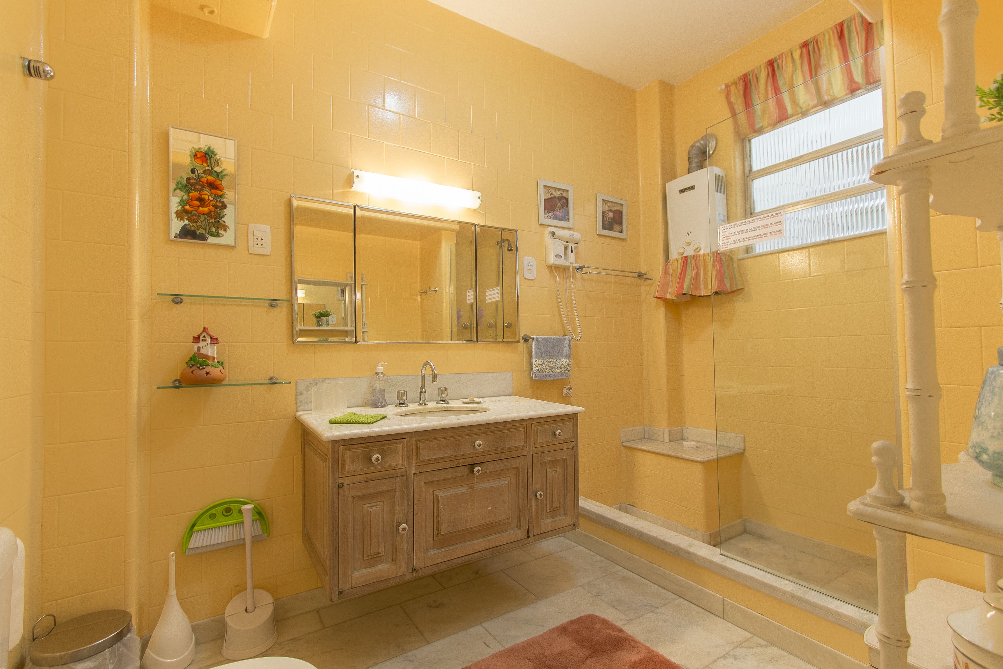 A bathroom with a yellow wall, a glass shower enclosure, a wooden vanity with a mirror, and a toilet.