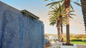 A building with a textured facade, palm trees, and a pathway leading to a water feature. - Luxury Villa #6550 on the grounds of Omni La Costa Resort & Spa-Newly Renovated! (Carlsbad)