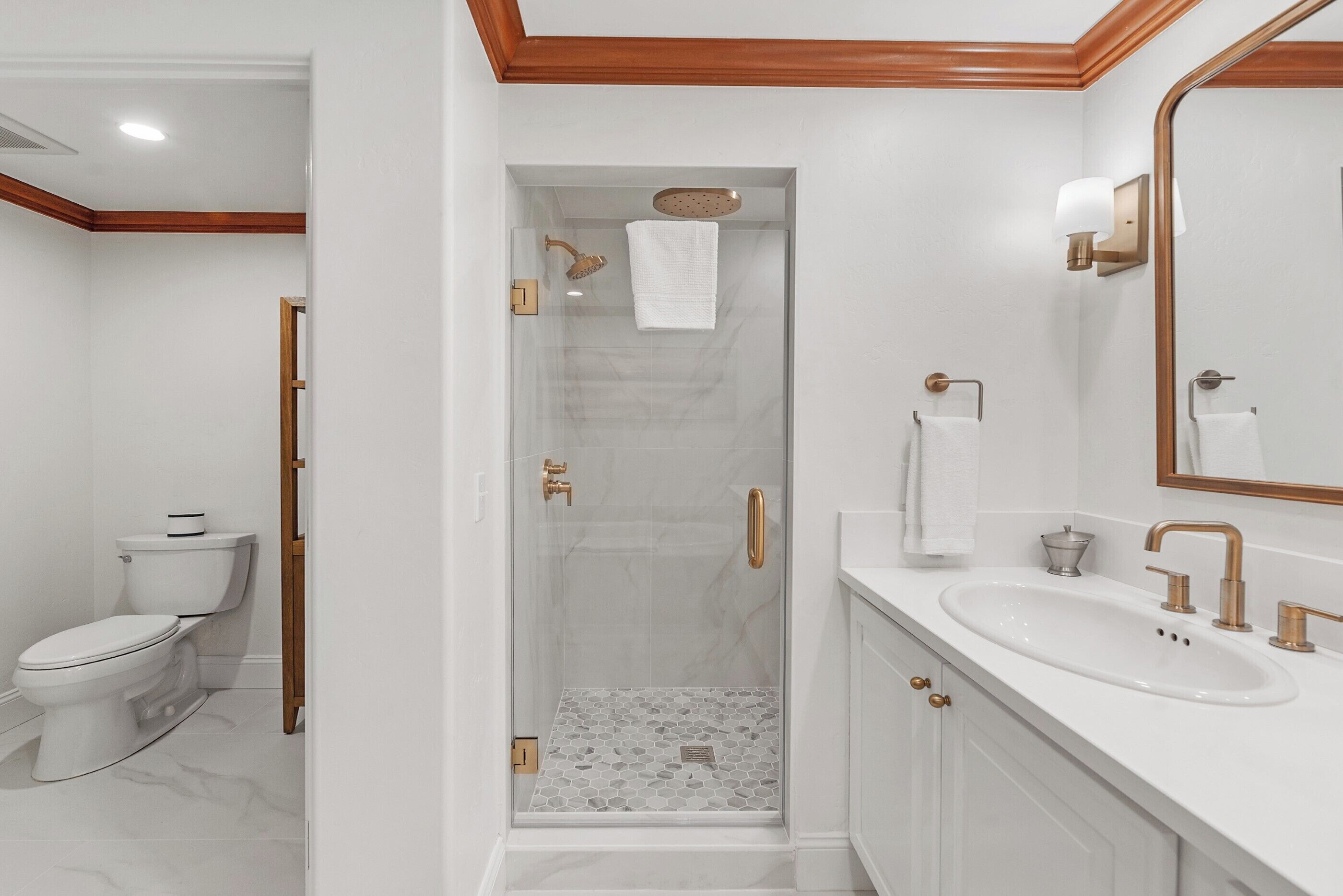 Une salle de bain moderne avec une douche à parois de verre, un lavabo blanc doté de robinetterie dorée et des toilettes.