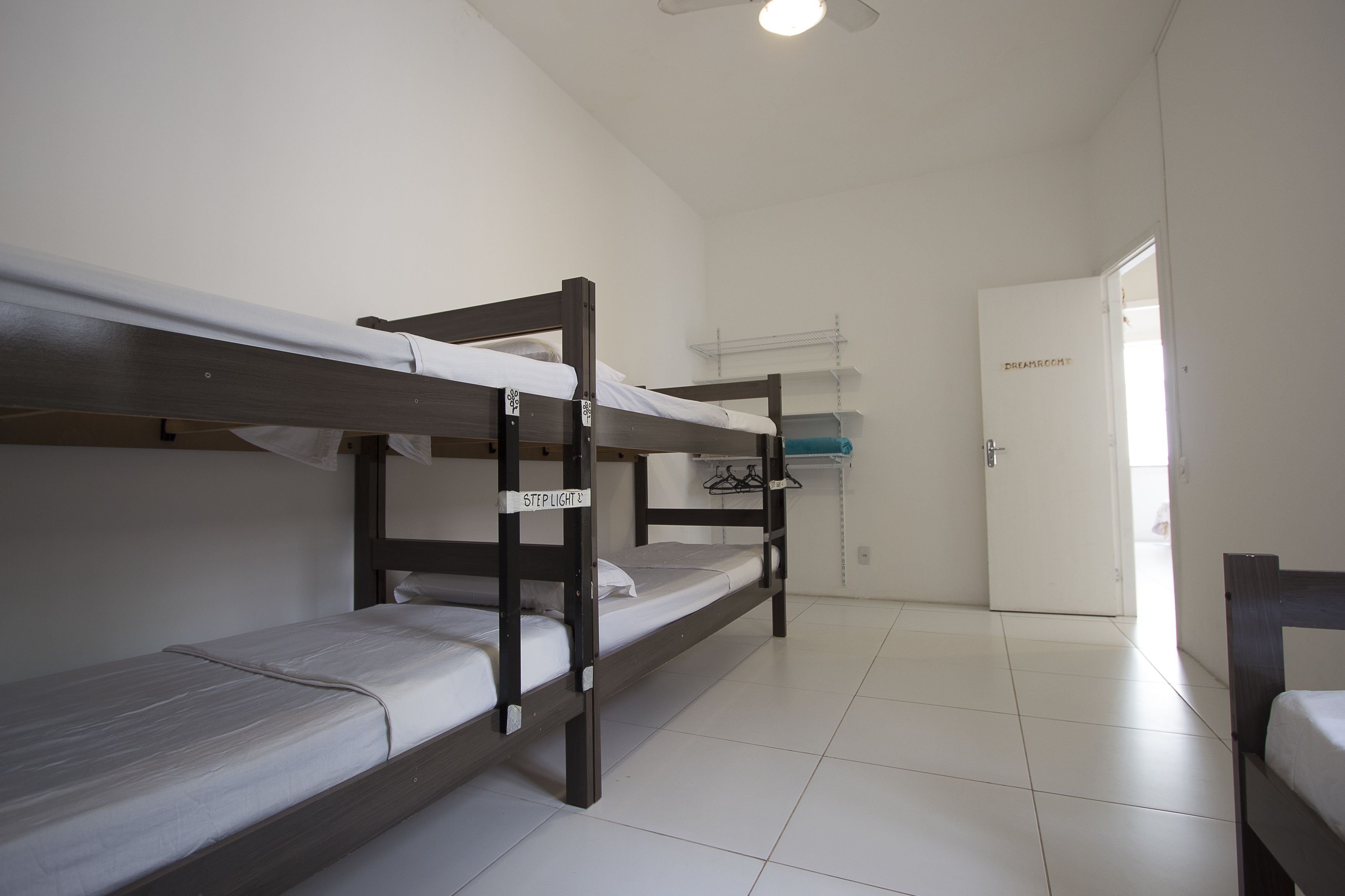 A dormitory room with two bunk beds, a white door, and a ceiling fan.