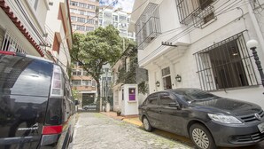 A narrow street with cobblestone pavement, parked cars, and buildings with balconies and barred windows. - LineRio Praia de Copacabana 372 (Rio de Janeiro)