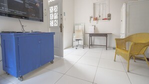A room with a large flat-screen TV mounted on the wall, a blue cabinet with wheels, a wicker chair, and a small table with a chair. - LineRio Praia de Copacabana 372 (Rio de Janeiro)