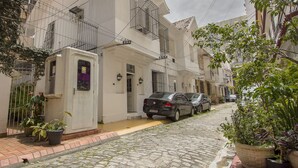 A narrow cobblestone street lined with white buildings, featuring balconies and potted plants. - LineRio Praia de Copacabana 372 (Rio de Janeiro)