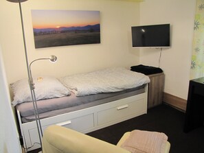 A small, neatly organized room with a single bed, a desk, a chair, a TV mounted on the wall, and a painting of a landscape. - Fine - Quiet - Convenient: Apartment "Hugo37" at the Bergpark (Bad Wilhelmshöhe)
