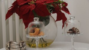 Ett bord med en vas av glas som innehåller röda julstjärneblommor, två glasklockor med bakverk och ett silverföremål i form av en rosett.