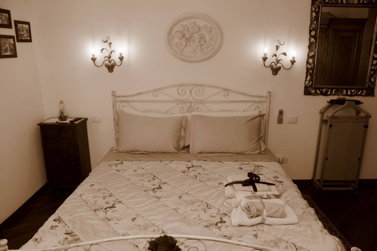 Un dormitorio con cama, mesita de noche, cómoda, espejo y apliques de pared.