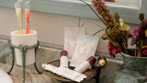 Ett badrum med en bänkskiva i marmor, ett ställ för tandborstar, en vas med blommor och ett bricka med toalettartiklar.