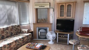 En kompakt opholdsstue med en sofa, et lille bord med en fjernbetjening, et fjernsyn og en ventilator.