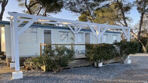 En campingvogn med hvid facade, en træterrasse og en grusvej.