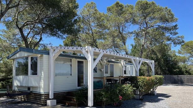 En campingvogn med veranda, omgivet af grus og træer.