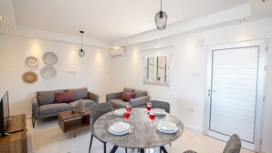 Una sala de estar moderna con una mesa de comedor redonda dispuesta para cuatro personas, dos sofás, un televisor y platos decorativos en la pared.