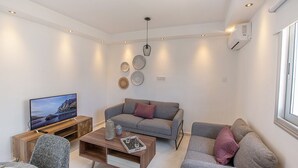 Una sala de estar moderna con un sofá gris, una mesa de centro de madera, un televisor sobre un mueble de madera y platos decorativos en la pared.