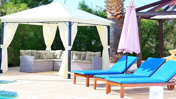 A covered outdoor seating area with a pool, lounge chairs, and a canopy. - Villa Artemisia (Coral Bay)