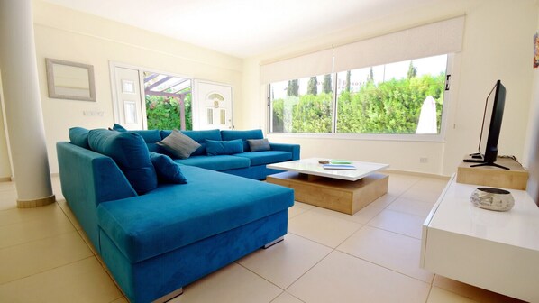 Ein modernes Wohnzimmer mit einem blauen Ecksofa, einem Couchtisch und einem Fernseher auf einem Lowboard.