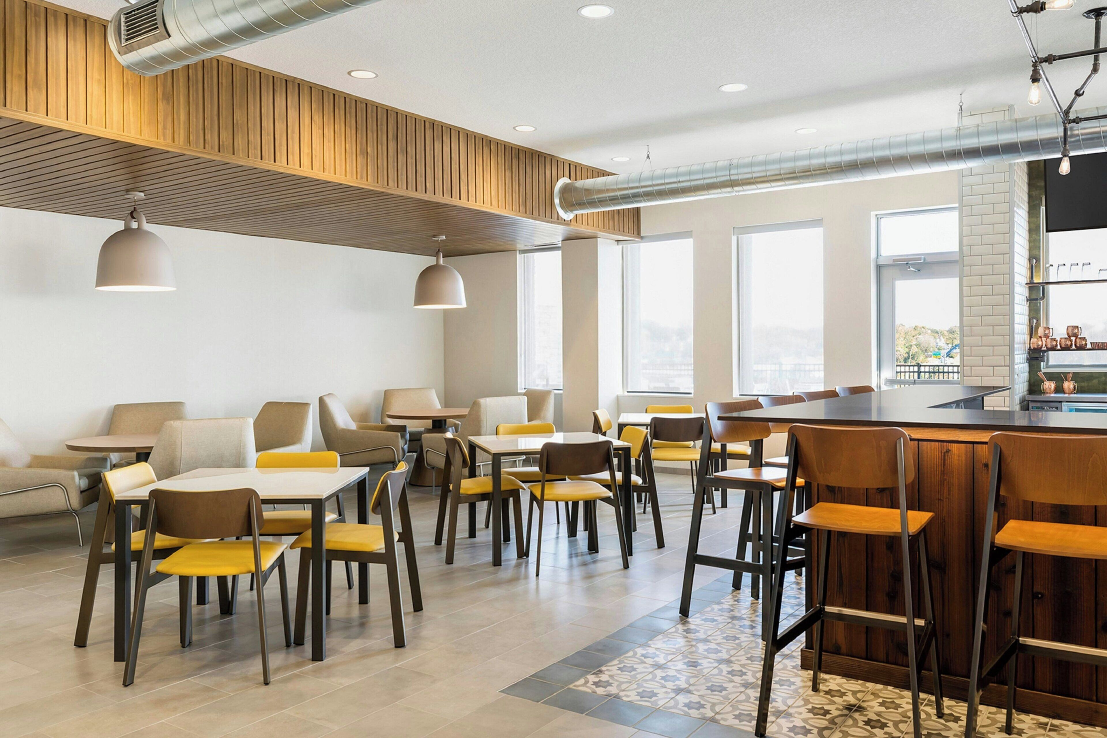 A modern dining area with tables and chairs, a bar counter, and large windows allowing natural light.