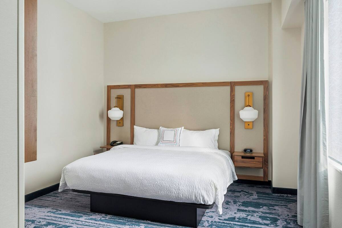 Une chambre d’hôtel avec un grand lit, deux tables de chevet, une tête de lit en bois et une moquette bleue à motifs.