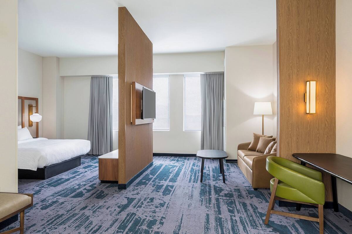 Une chambre d’hôtel avec un lit, un bureau, une chaise verte, un canapé et un téléviseur.