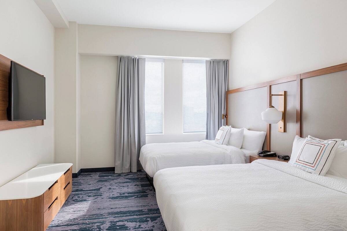 Une chambre d’hôtel avec deux lits, une télévision, une table de chevet et une fenêtre avec des rideaux.