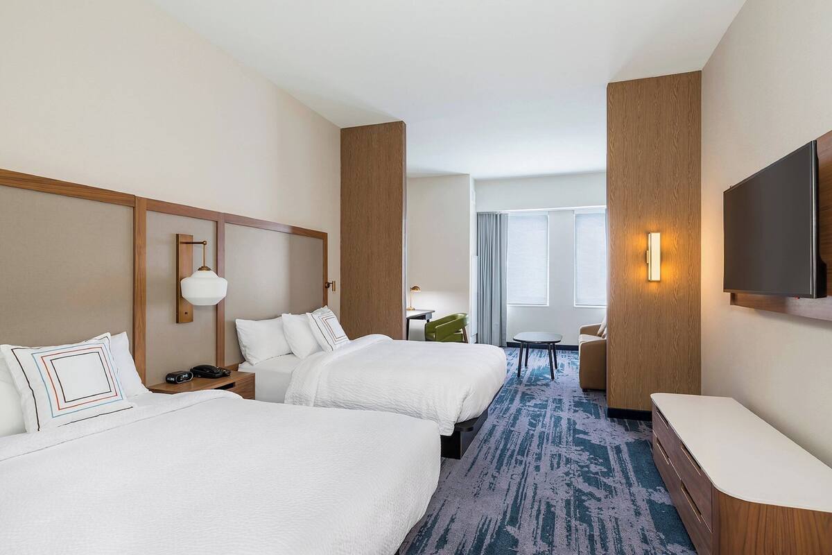 Une chambre d’hôtel avec deux lits, un bureau, une chaise, une télévision et une grande fenêtre.