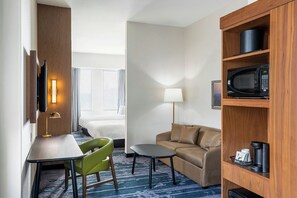 A hotel room with a bed, a desk with a chair, a sofa, a coffee table, a lamp, a microwave, and a TV.