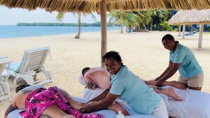 A beachside massage area with a thatched roof, a massage table, and a chair. - Luxury Beachfront Cabana with swim up pool bar (Placencia)