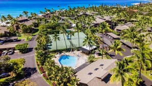 An aerial view of a resort with multiple buildings, a swimming pool, and a tennis court surrounded by palm trees. - Kanaloa at Kona 3304: Delightful Oceanfront Condo w/ AC, Pool & Spa (Kailua Kona)