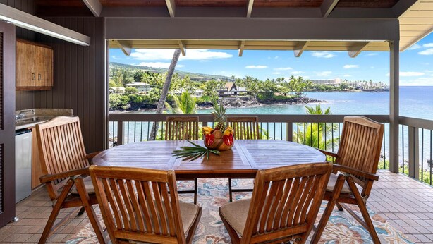 A wooden table with chairs on a balcony overlooking a coastal view. - Kanaloa at Kona 3304: Delightful Oceanfront Condo w/ AC, Pool & Spa (Kailua Kona)