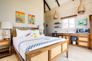 Un dormitorio con una cama de madera, una mesita de noche, una lámpara y una mesilla. Se ve una ventana con vistas al exterior.