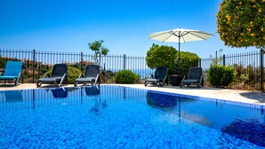 A clear blue pool with lounge chairs and an umbrella, surrounded by a fence and greenery. - Stunning 3 bedroom villa 'BZ01' with private pool, stunning views, communal pool and resort facilities, Zephyros Village on Aphrodite Hills Re (Kouklia)