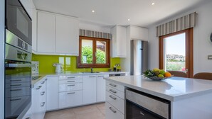 A modern kitchen with white cabinets, a stainless steel dishwasher, and a window with a view of greenery. - Stunning 3 bedroom villa 'BZ01' with private pool, stunning views, communal pool and resort facilities, Zephyros Village on Aphrodite Hills Re (Kouklia)