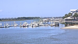 A marina with boats docked, a bridge in the background, and a building with a beach in the foreground.