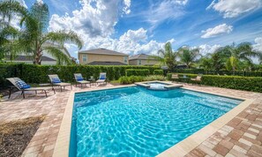 A rectangular swimming pool with a hot tub, surrounded by lounge chairs and a brick patio. - 6BR Encore Villa | Themed Rooms & Private Pool (Kissimmee)