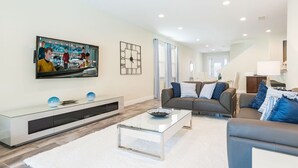 Een moderne woonkamer met een flatscreen televisie, een glazen salontafel, een bank en een witte televisiemeubel.