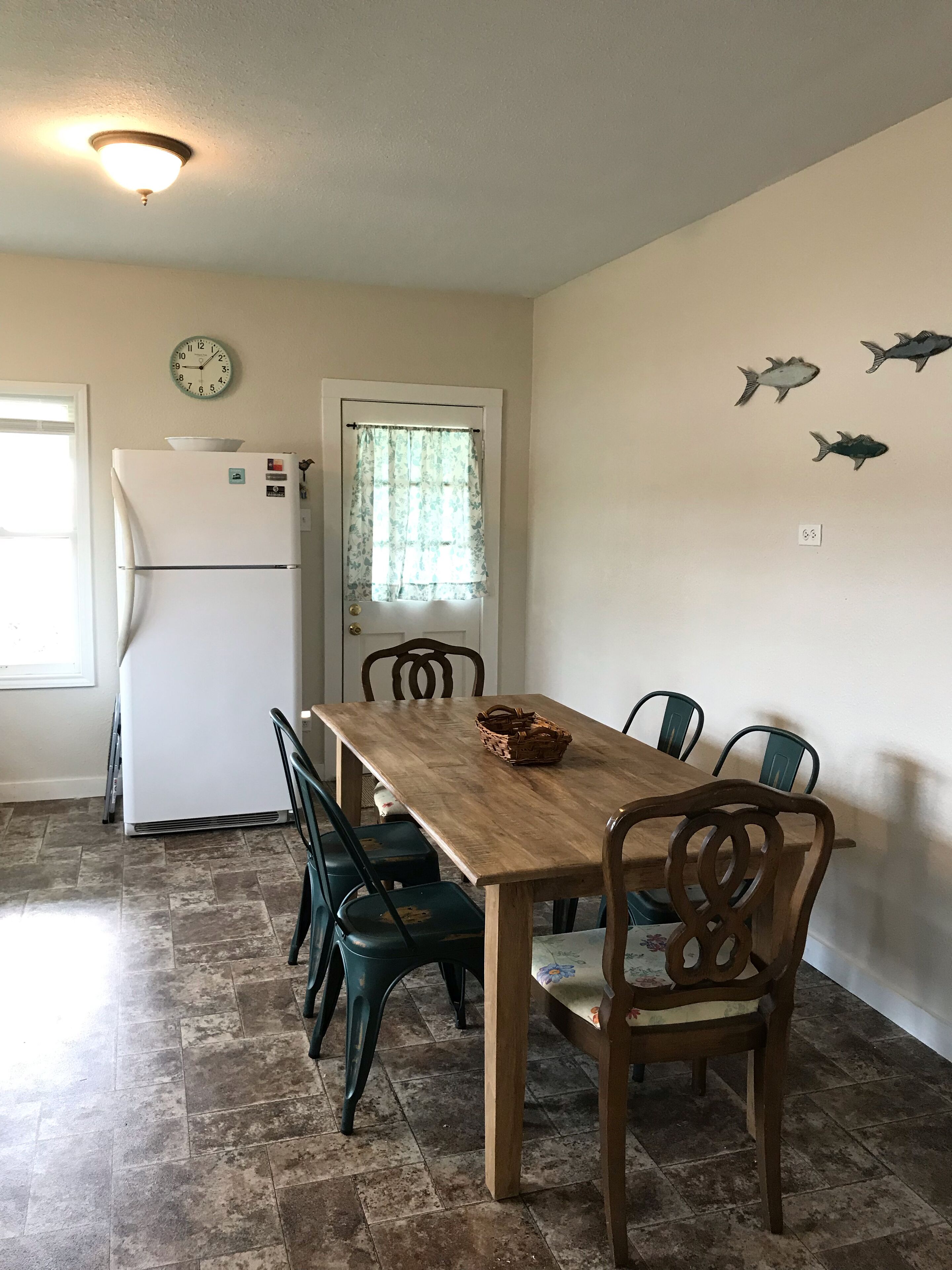 Un comedor con una mesa y sillas de madera, un refrigerador, un reloj y decoración de peces en la pared.