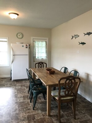 A dining area with a wooden table and chairs, a refrigerator, a clock, and decorative fish wall art. - Charming House 1/2 Block from Bay (Fulton)