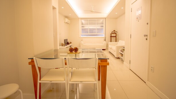 Une pièce moderne et bien éclairée, avec une table à manger en verre, des chaises blanches, un canapé et un ventilateur de plafond.