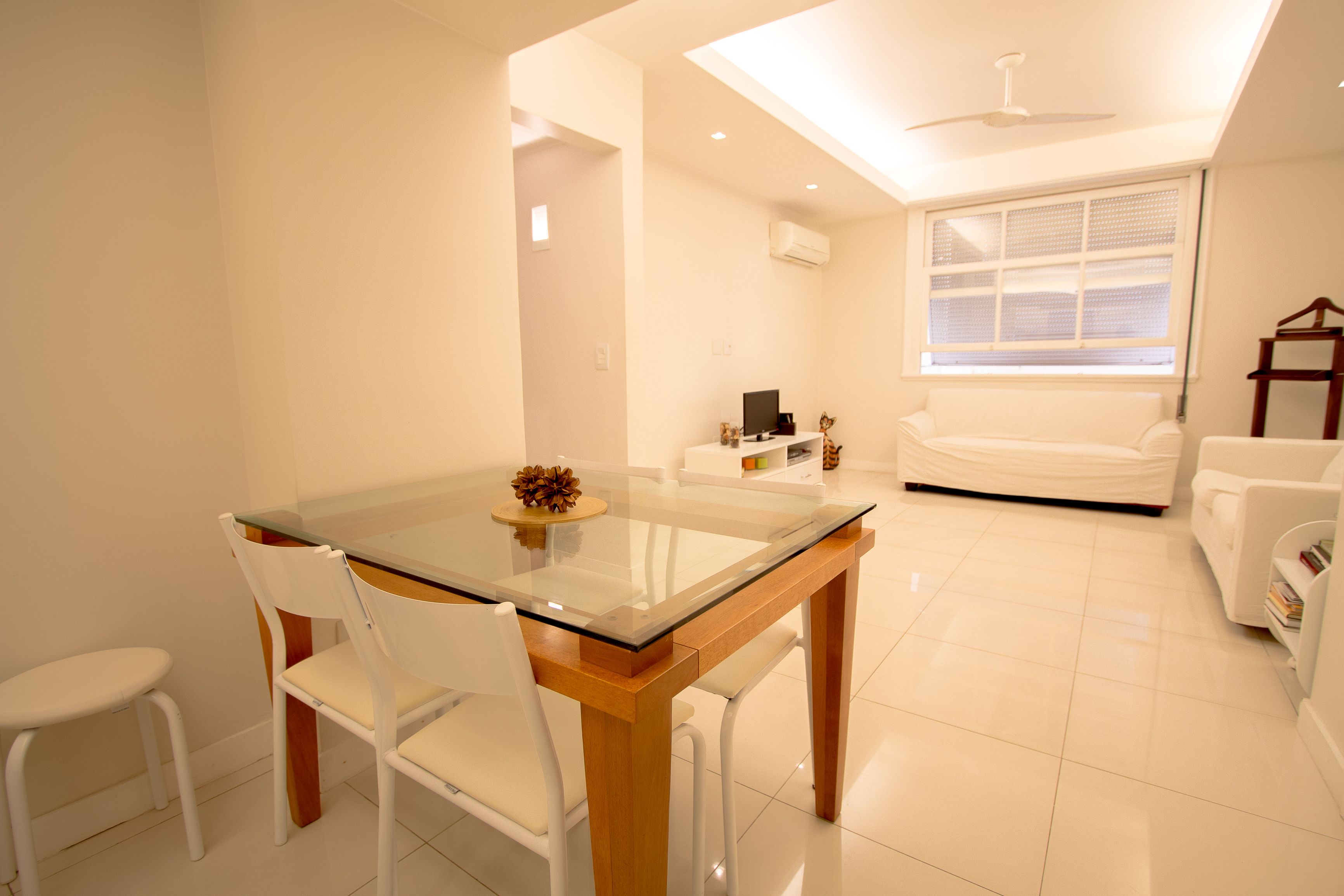A modern living room with a glass dining table, white chairs, a sofa, and a TV.