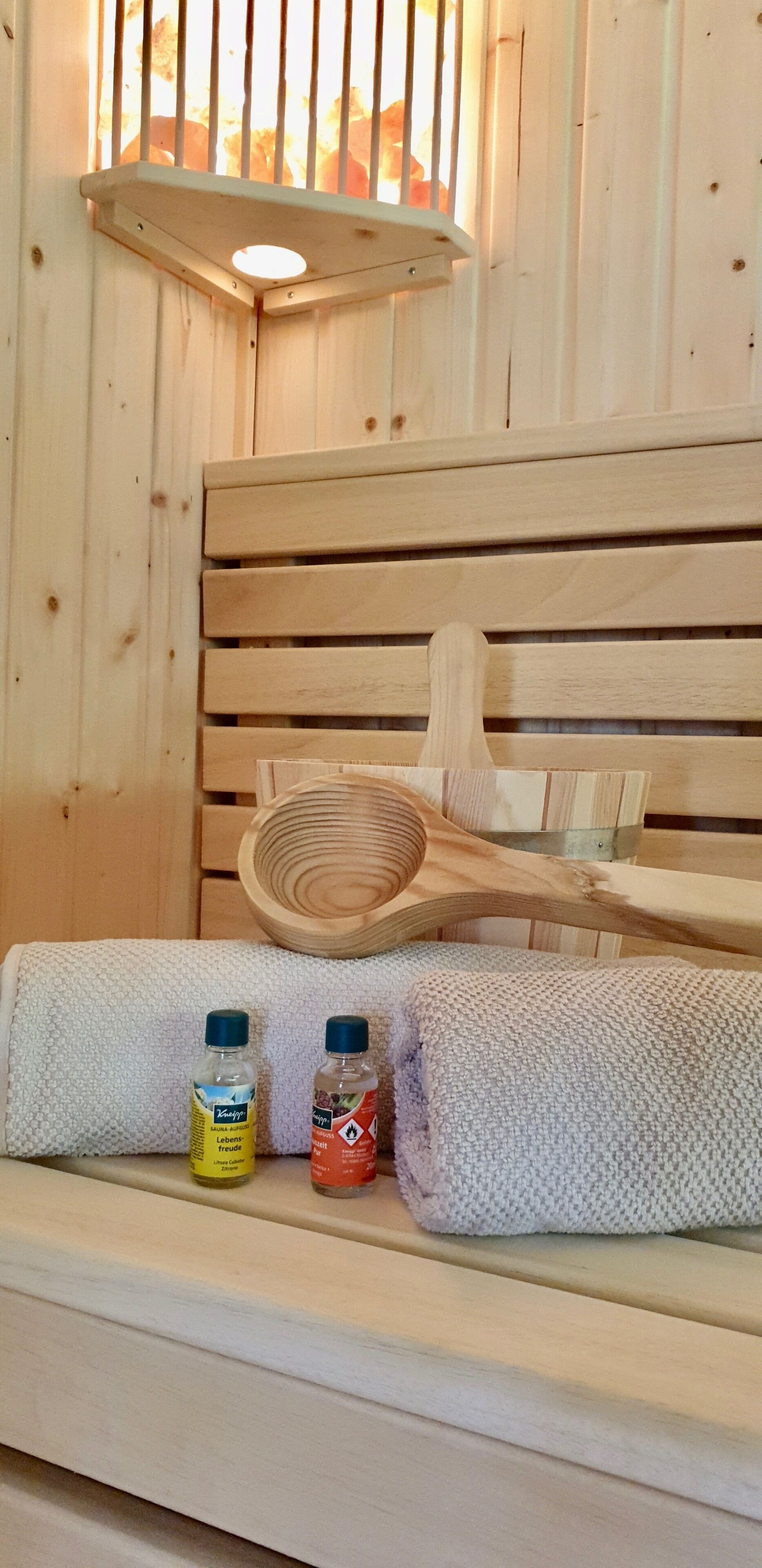 En träbänk med en vävd handduk och två flaskor badsalt placerade i en stuga med träinredning.