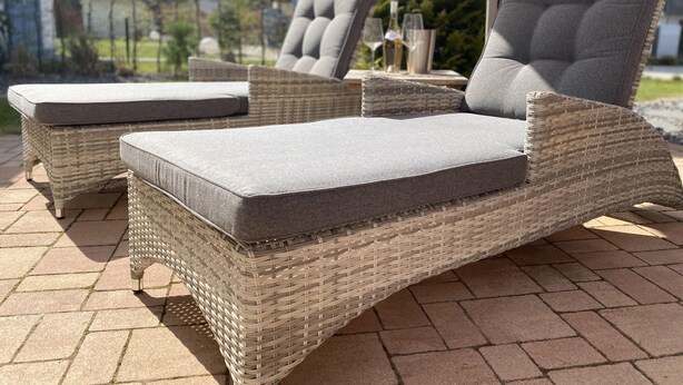 Wicker lounge chairs with grey cushions on a paved patio.