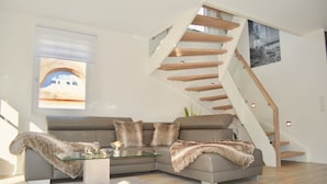 A modern living room with a glass coffee table, a grey sectional sofa, and a wooden staircase.