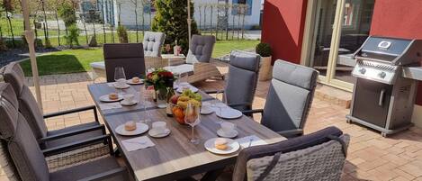An outdoor dining area with a table set for two, surrounded by wicker chairs.