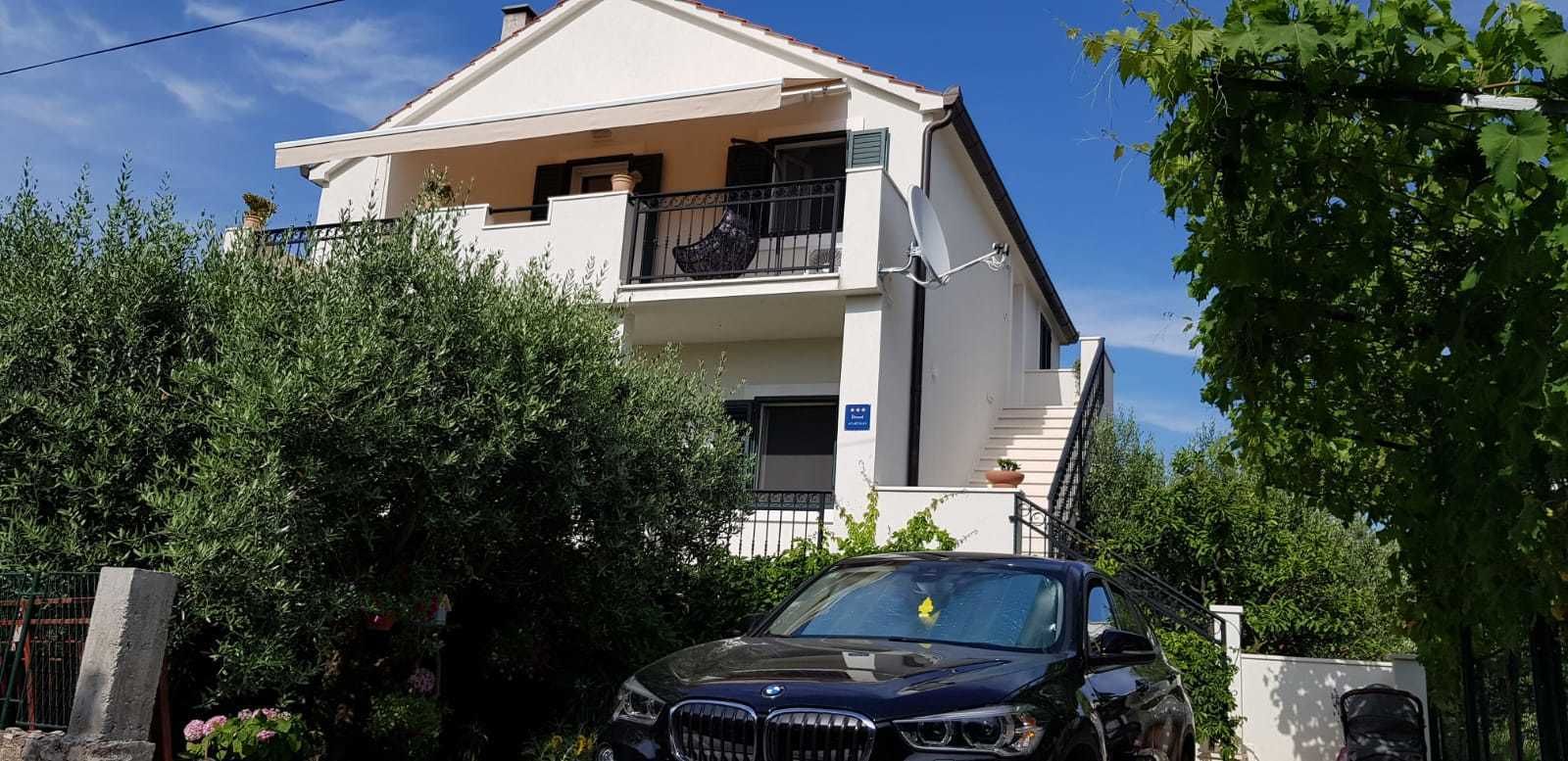A two-story residential building with a balcony, a satellite dish, and a car parked in front.