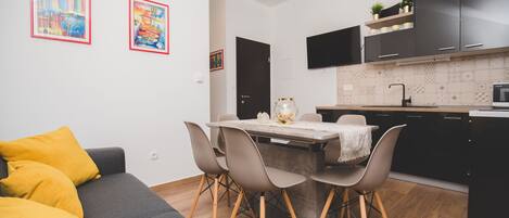 A modern kitchen with black cabinets, a dining table with chairs, and a grey sofa with yellow cushions.