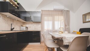 Une cuisine moderne avec des meubles de couleur noire, une table à manger avec des chaises et une fenêtre ornée de rideaux légers.