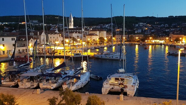 Un port de plaisance au crépuscule, avec de nombreux bateaux amarrés, une église en arrière-plan et une ville de l’autre côté de l’eau.